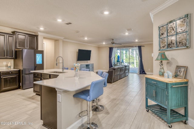 kitchen with crown molding, sink, a center island with sink, stainless steel refrigerator, and a breakfast bar area