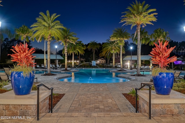 pool at night featuring pool water feature and a patio