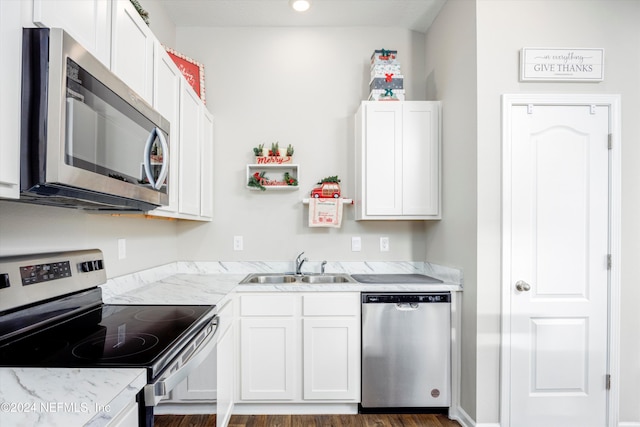 kitchen featuring appliances with stainless steel finishes, light stone counters, sink, dark hardwood / wood-style floors, and white cabinetry