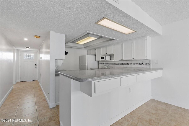 kitchen with light tile patterned flooring, kitchen peninsula, a textured ceiling, white appliances, and white cabinets