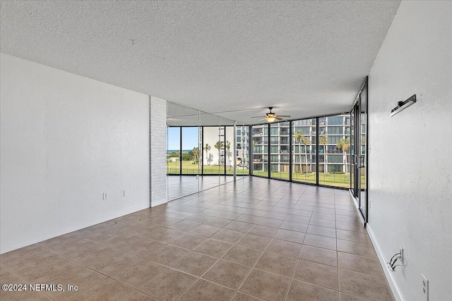 unfurnished room featuring floor to ceiling windows, ceiling fan, light tile patterned floors, and a textured ceiling