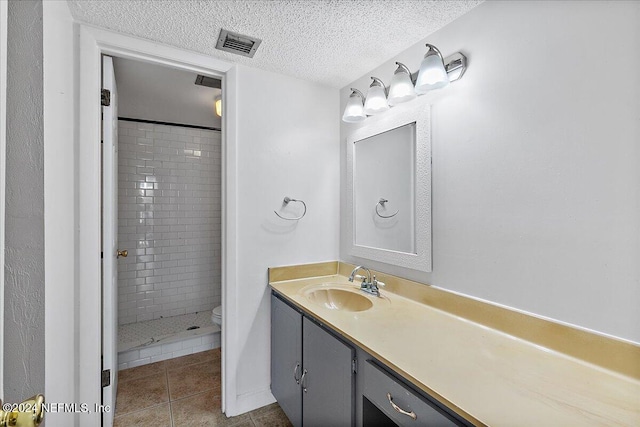 bathroom featuring tile patterned floors, a textured ceiling, toilet, tiled shower, and vanity