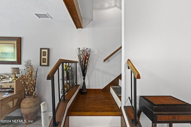 stairs featuring beamed ceiling, a textured ceiling, and tile patterned flooring