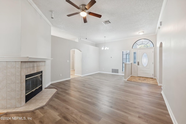 unfurnished living room featuring ceiling fan with notable chandelier, light wood-type flooring, a textured ceiling, and ornamental molding