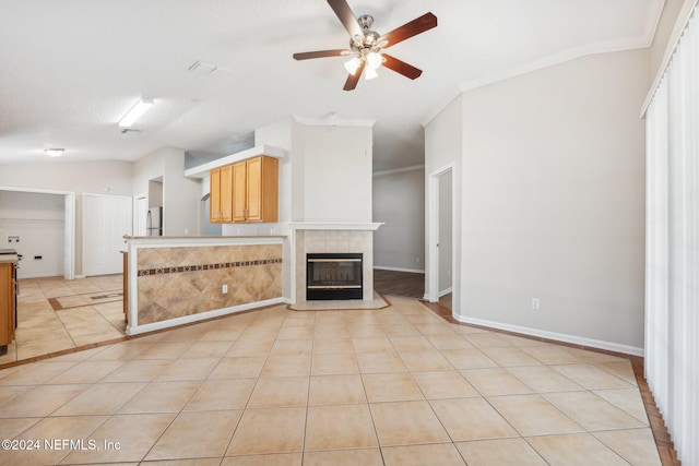 unfurnished living room featuring light tile patterned floors, vaulted ceiling, crown molding, and a tiled fireplace