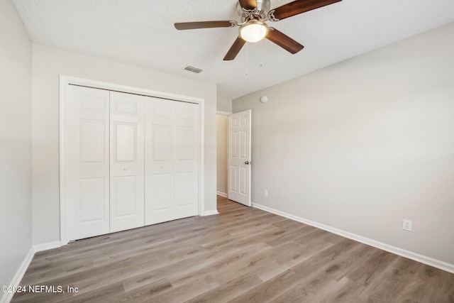 unfurnished bedroom featuring a textured ceiling, a closet, light hardwood / wood-style floors, and ceiling fan