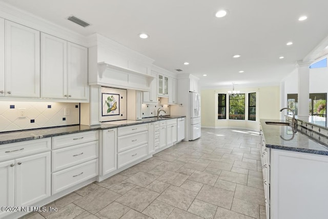 kitchen with sink, backsplash, dark stone countertops, white fridge, and white cabinets