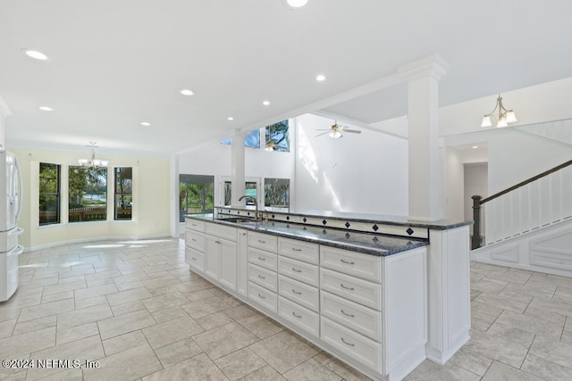 kitchen featuring ceiling fan, an island with sink, pendant lighting, dark stone counters, and white cabinets