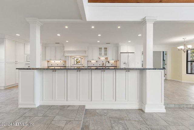 kitchen featuring white refrigerator with ice dispenser, white cabinetry, dark stone counters, and a notable chandelier