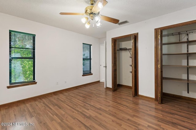 unfurnished bedroom with two closets, ceiling fan, dark wood-type flooring, and a textured ceiling