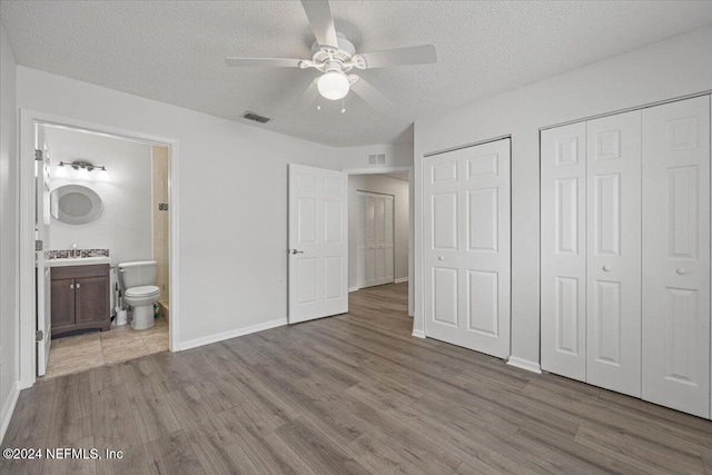 unfurnished bedroom with hardwood / wood-style floors, connected bathroom, a textured ceiling, and ceiling fan