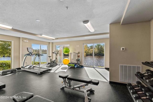 gym featuring a water view, a healthy amount of sunlight, and a textured ceiling