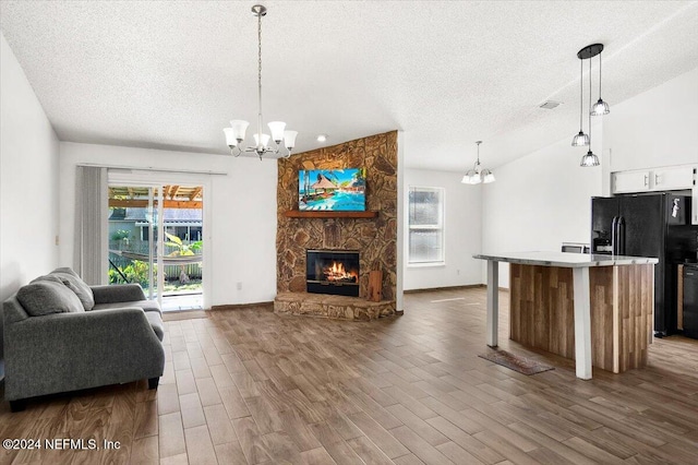 living room featuring a stone fireplace, wood-type flooring, a textured ceiling, and a wealth of natural light