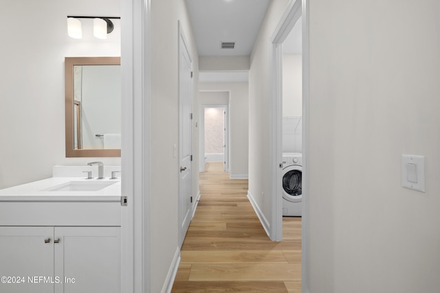 corridor with sink, light hardwood / wood-style floors, and washer / dryer