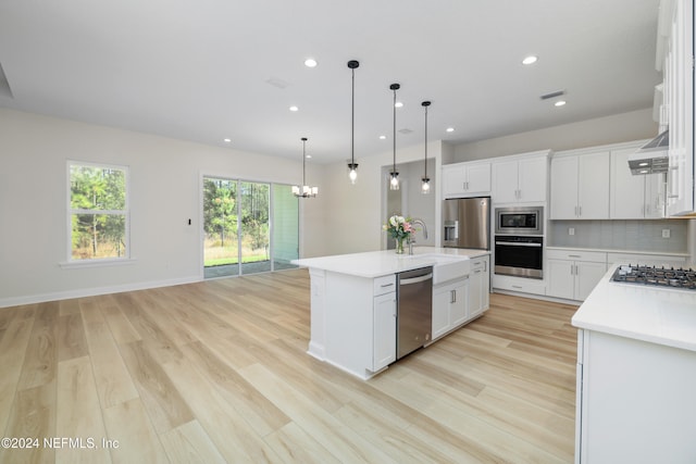 kitchen with a kitchen island with sink, light hardwood / wood-style flooring, decorative light fixtures, white cabinetry, and stainless steel appliances