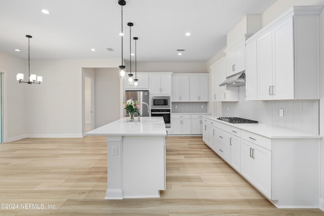 kitchen featuring hanging light fixtures, light hardwood / wood-style flooring, an island with sink, appliances with stainless steel finishes, and white cabinetry