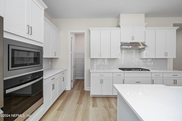 kitchen featuring white cabinets, decorative backsplash, light wood-type flooring, and stainless steel appliances