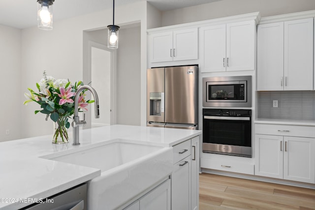 kitchen featuring white cabinets, sink, light wood-type flooring, appliances with stainless steel finishes, and decorative light fixtures