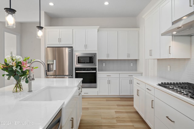 kitchen with appliances with stainless steel finishes, backsplash, extractor fan, pendant lighting, and white cabinetry