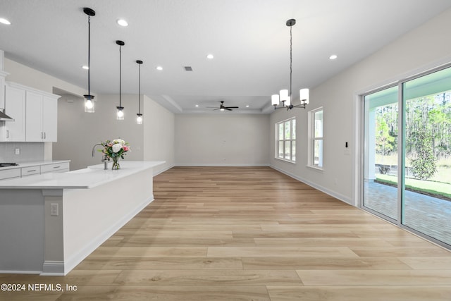 kitchen with pendant lighting, ceiling fan with notable chandelier, light hardwood / wood-style floors, and white cabinetry