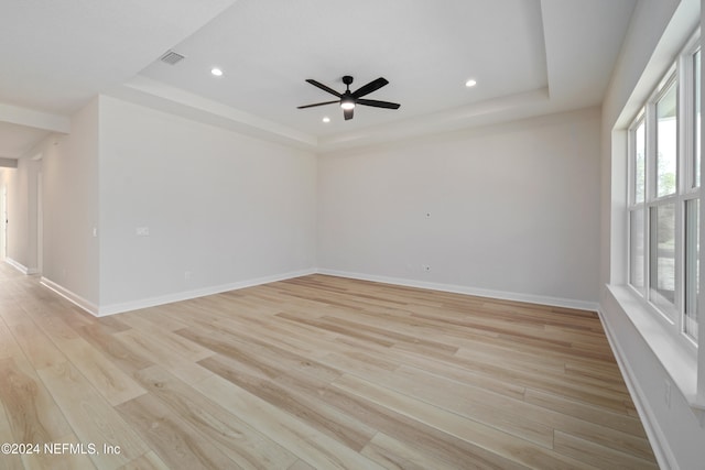 empty room with ceiling fan, a tray ceiling, and light hardwood / wood-style flooring