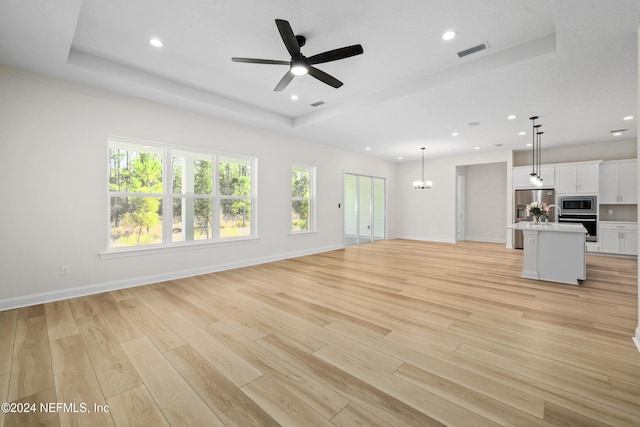 unfurnished living room with a raised ceiling, light hardwood / wood-style flooring, and ceiling fan with notable chandelier