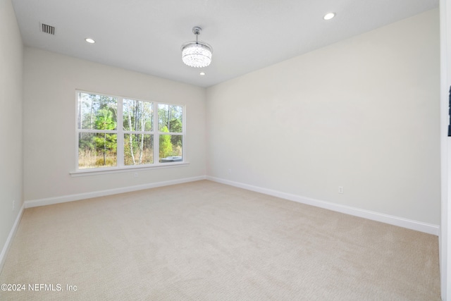 unfurnished room featuring light colored carpet and a chandelier