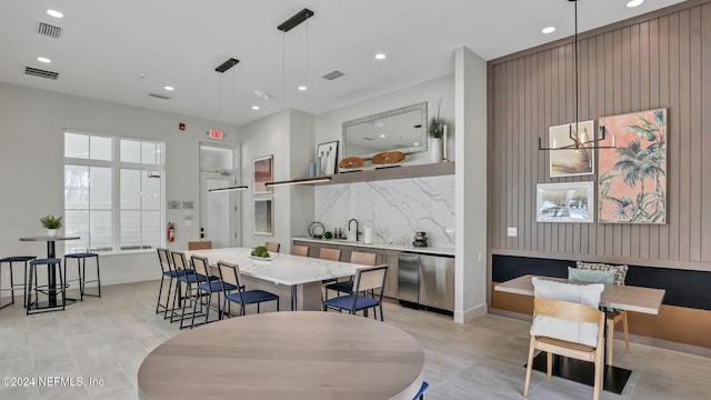 interior space featuring stainless steel dishwasher, decorative backsplash, light stone countertops, decorative light fixtures, and a kitchen island