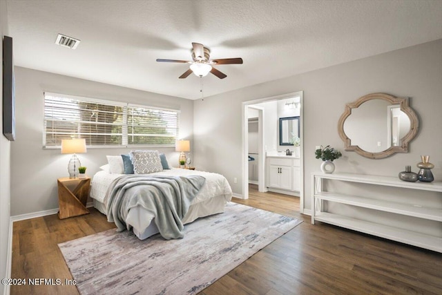 bedroom with ensuite bath, ceiling fan, sink, dark hardwood / wood-style flooring, and a textured ceiling