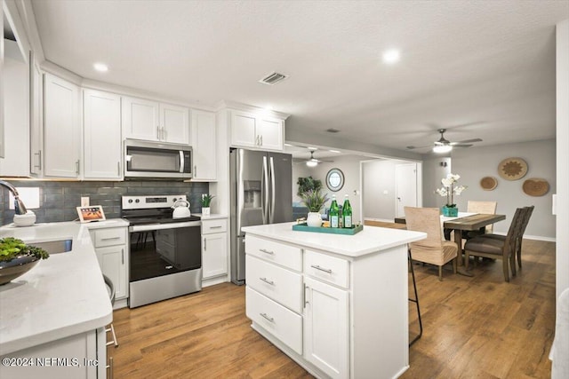 kitchen with appliances with stainless steel finishes, white cabinetry, a kitchen island, and wood-type flooring