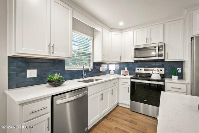 kitchen featuring white cabinetry, sink, backsplash, light hardwood / wood-style floors, and appliances with stainless steel finishes