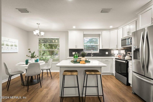 kitchen with stainless steel appliances, hardwood / wood-style flooring, a center island, white cabinetry, and hanging light fixtures