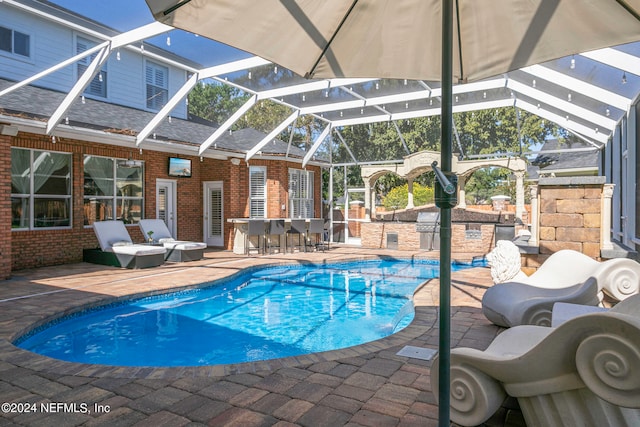 view of pool with a patio, an outdoor bar, a lanai, and exterior kitchen