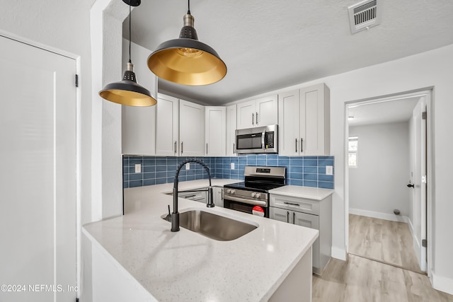 kitchen with white cabinets, sink, light hardwood / wood-style flooring, appliances with stainless steel finishes, and light stone counters