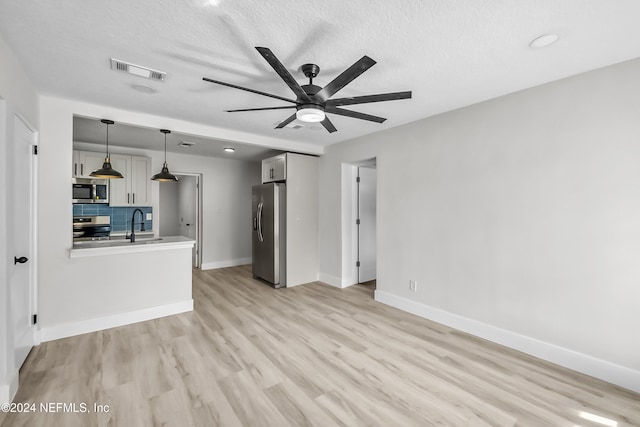 unfurnished living room featuring ceiling fan, sink, light hardwood / wood-style floors, and a textured ceiling