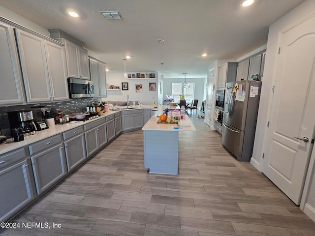 kitchen featuring gray cabinetry, a center island, sink, hanging light fixtures, and stainless steel appliances