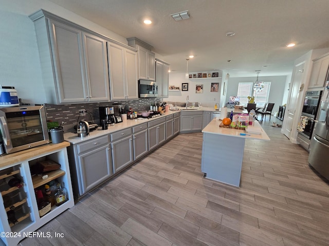 kitchen featuring gray cabinetry, sink, hanging light fixtures, light hardwood / wood-style floors, and appliances with stainless steel finishes