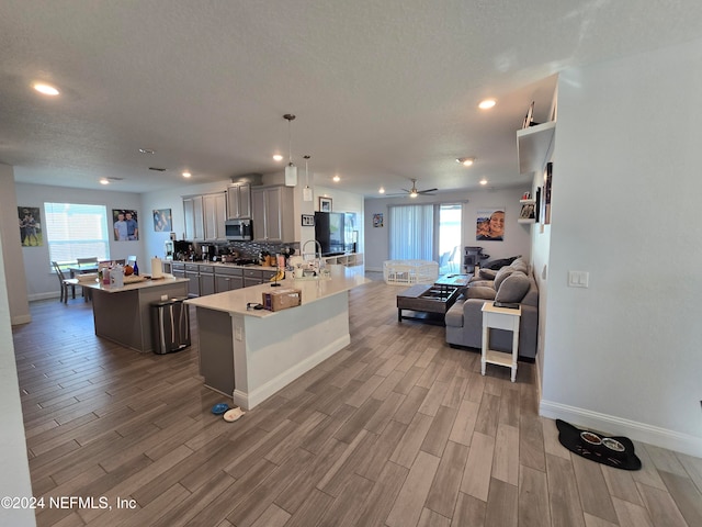 kitchen featuring gray cabinetry, an island with sink, hanging light fixtures, and hardwood / wood-style flooring