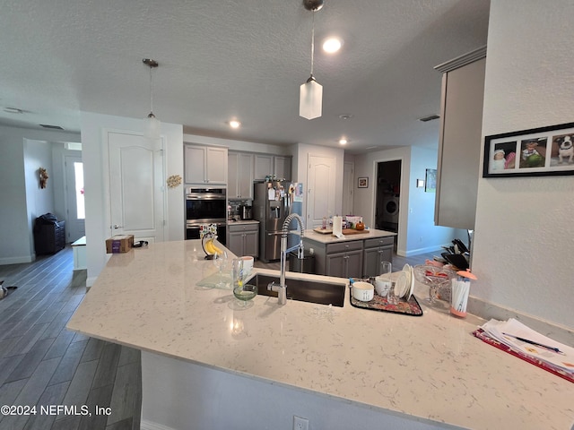 kitchen with gray cabinetry, sink, hanging light fixtures, dark hardwood / wood-style floors, and stainless steel appliances