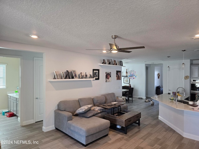 living room featuring ceiling fan, light hardwood / wood-style flooring, a textured ceiling, and sink