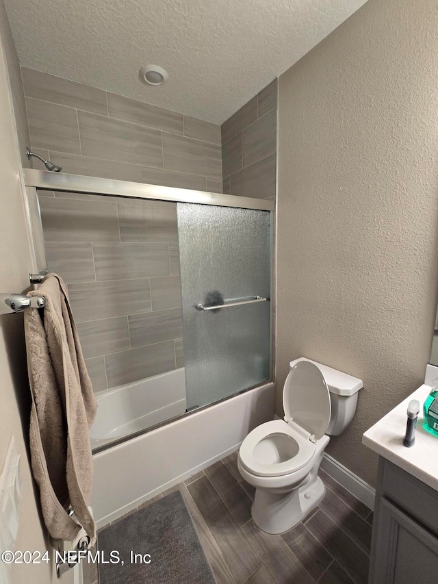 full bathroom with toilet, combined bath / shower with glass door, a textured ceiling, and vanity