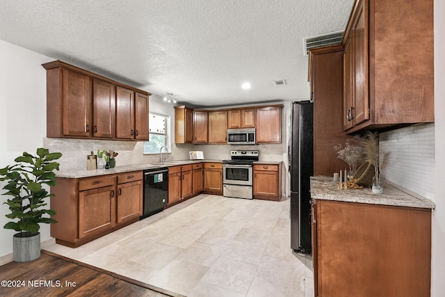 kitchen featuring a textured ceiling, sink, light stone countertops, and stainless steel appliances