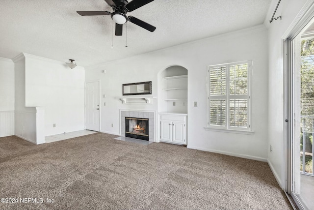 unfurnished living room featuring ceiling fan, ornamental molding, a fireplace, a textured ceiling, and light colored carpet