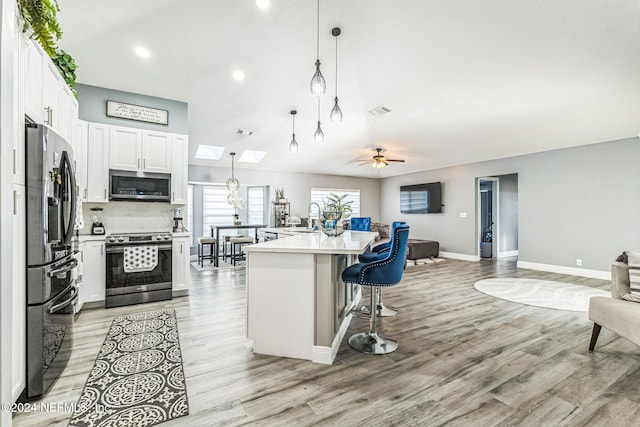 kitchen with a skylight, ceiling fan, hanging light fixtures, stainless steel appliances, and white cabinets