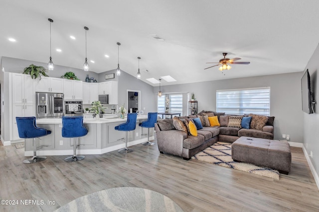 living room featuring ceiling fan, vaulted ceiling with skylight, and light hardwood / wood-style flooring