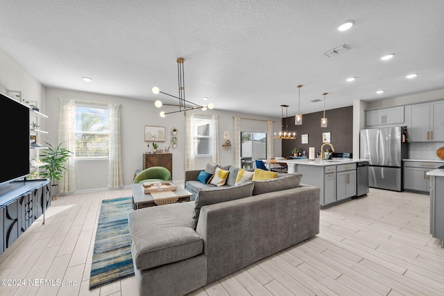 living room featuring sink, an inviting chandelier, a textured ceiling, and light hardwood / wood-style flooring