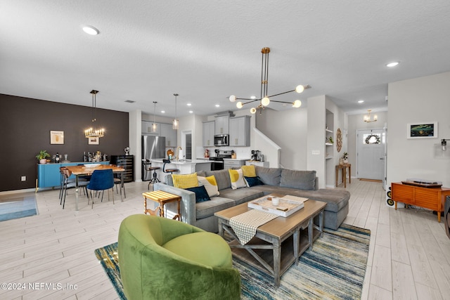 living room with light hardwood / wood-style floors, a textured ceiling, and an inviting chandelier