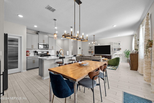 dining room with light wood-type flooring, a textured ceiling, a chandelier, and sink