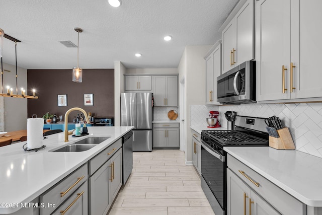 kitchen with hanging light fixtures, sink, decorative backsplash, gray cabinets, and appliances with stainless steel finishes