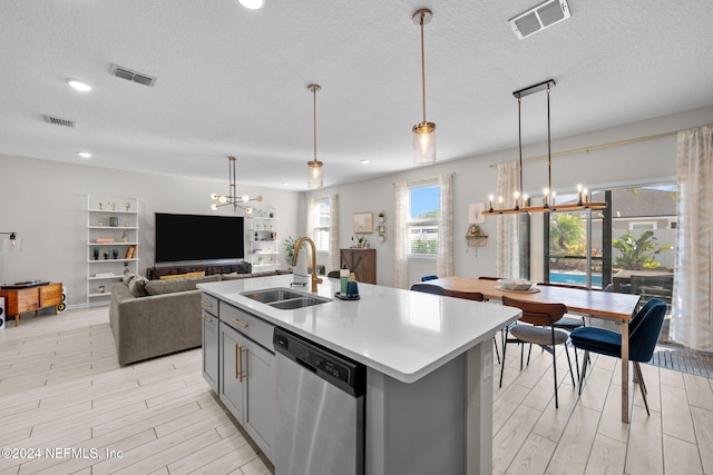 kitchen featuring a kitchen island with sink, sink, decorative light fixtures, dishwasher, and light hardwood / wood-style floors